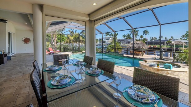A glass-enclosed dining area with a view of a swimming pool and palm trees. - Elegant 4-BR Tempur Pedic w/ Pvt Pool & Beach Access (Cape Coral)