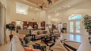 A spacious living area with a large sofa, coffee table, and a dining area with a kitchen in the background. - Elegant 4-BR Tempur Pedic w/ Pvt Pool & Beach Access (Cape Coral)