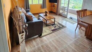 A spacious living room with a wooden ceiling, a black sofa, a coffee table, and a TV on a stand.