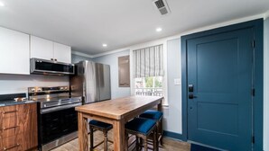 Une cuisine moderne dotée d’appareils électroménagers en acier inoxydable, d’un îlot central en bois avec des tabourets de bar et d’une porte bleue.