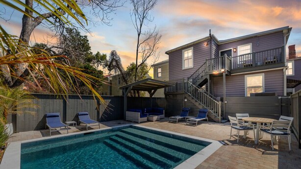 Un jardin avec une piscine, des chaises longues, un patio couvert et une maison à deux étages dotée d’un balcon.