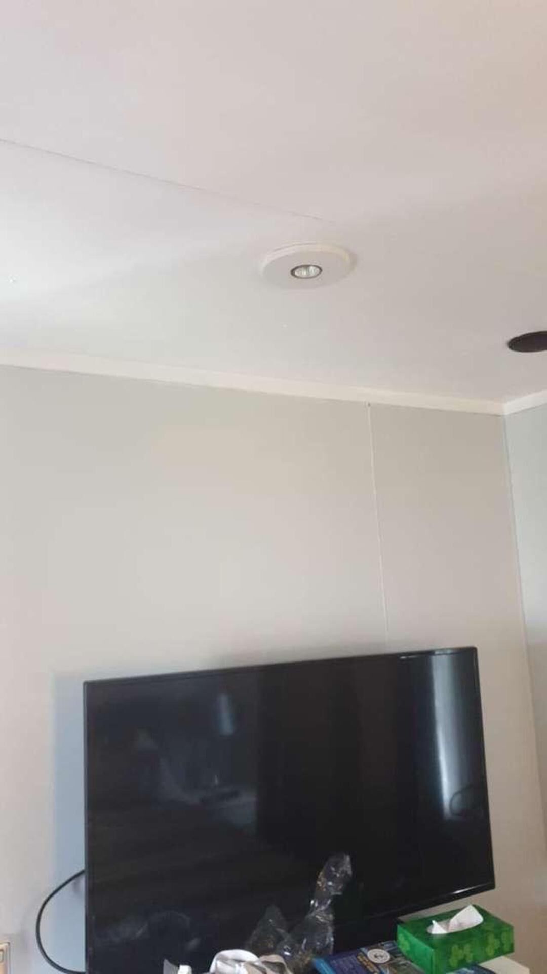 A room with a flat-screen TV, a green tissue box, and a white wall.