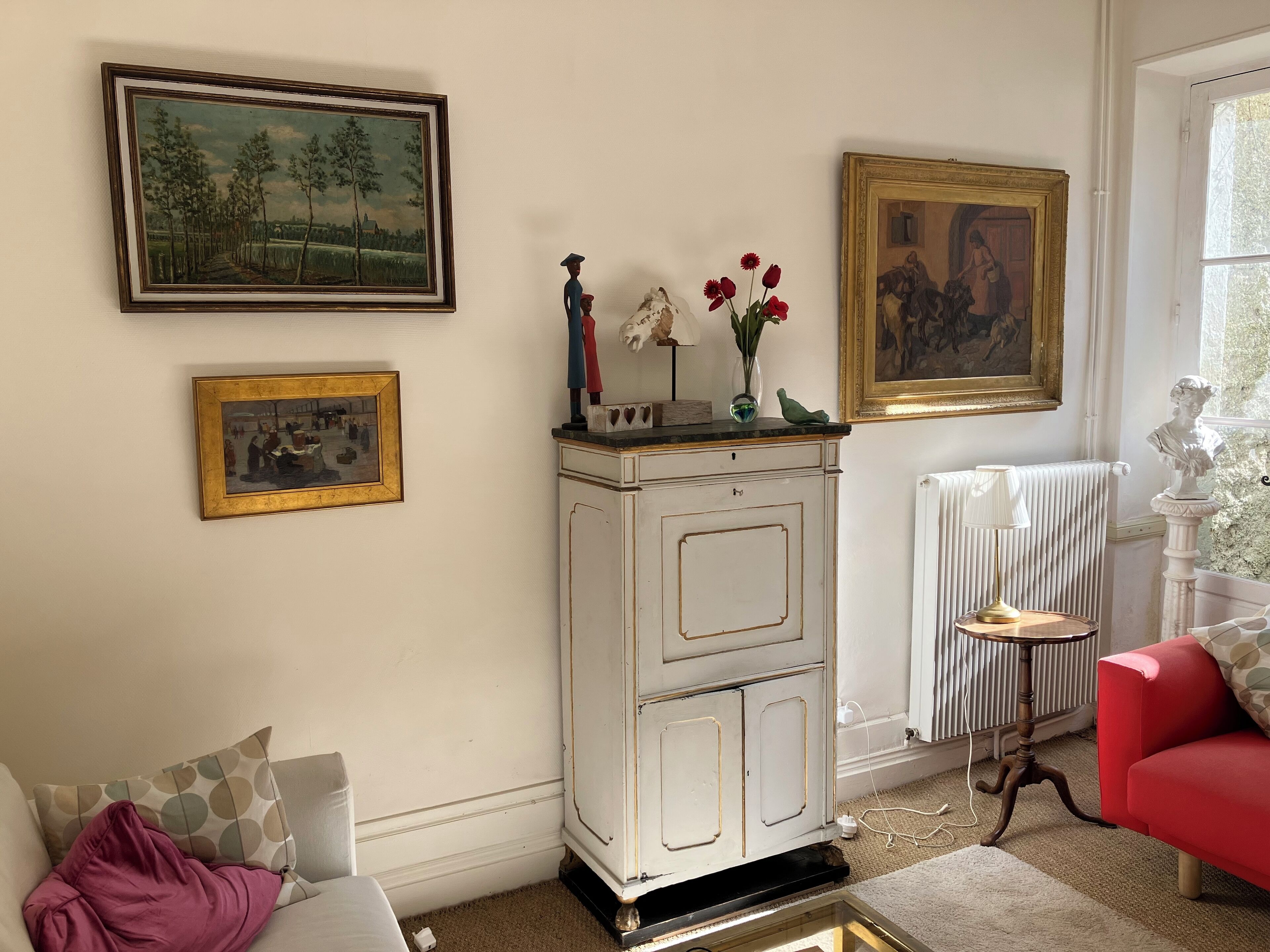 A living room with a white cabinet, a red sofa, and two framed paintings on the wall.