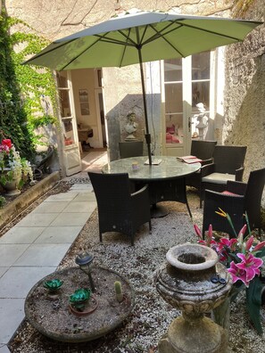 Eine Terrasse mit rundem Tisch, Stühlen, einem Sonnenschirm und Kübelpflanzen.