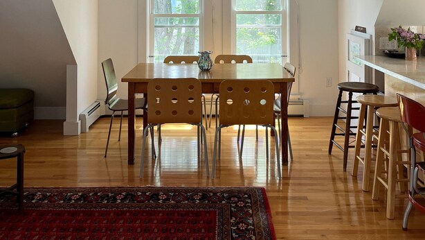 A dining area with a wooden table and chairs, a chandelier, and large windows.