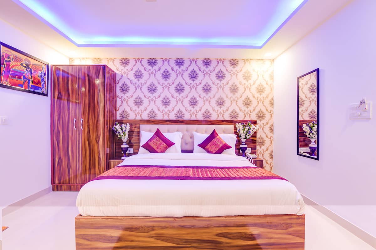 A bedroom with a large bed, wooden wardrobe, patterned wallpaper, and a mirror on the wall.