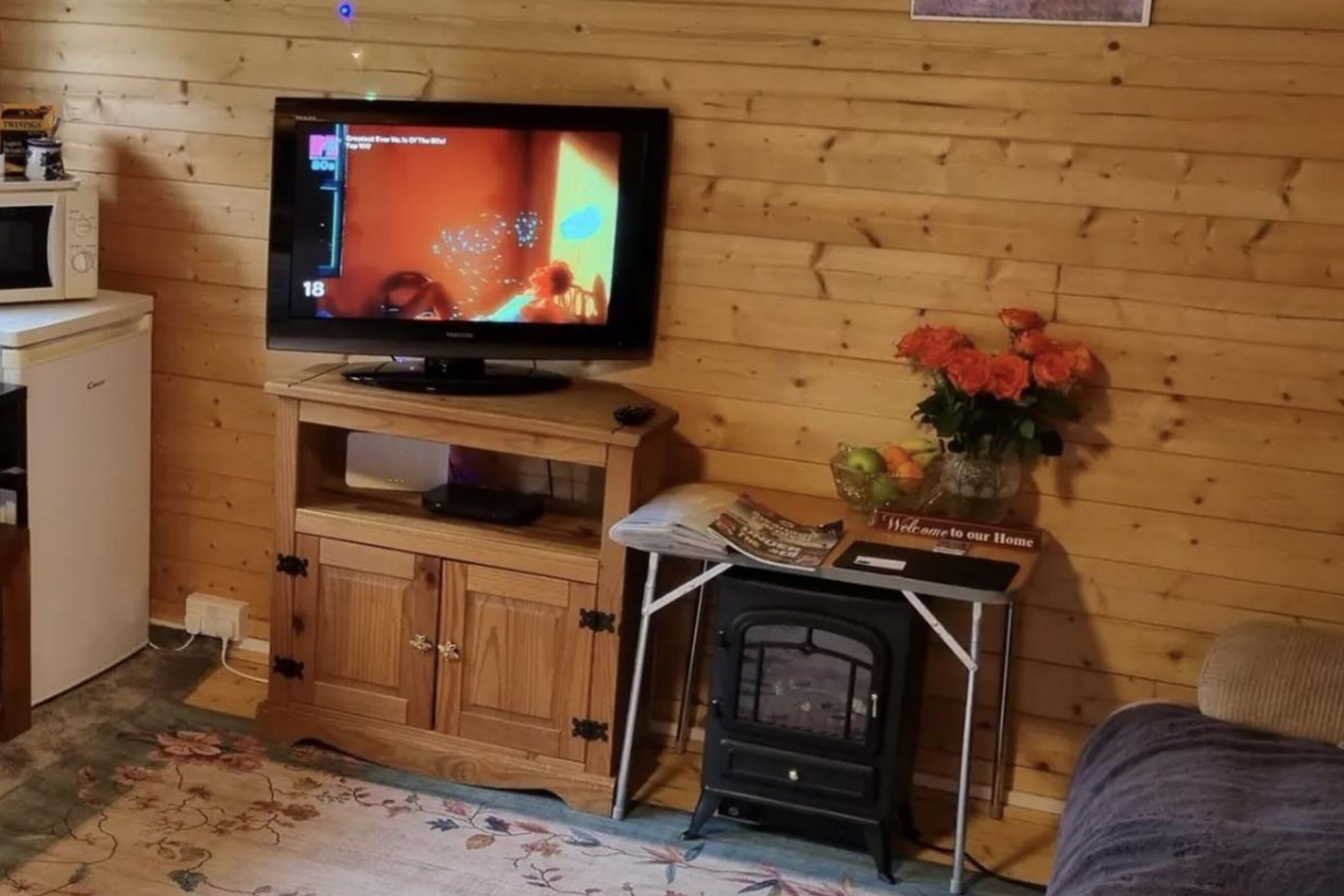 Une pièce confortable avec un mur en bois, une télévision, une petite table ornée d’un vase de fleurs, un four à micro-ondes et une cuisinière.