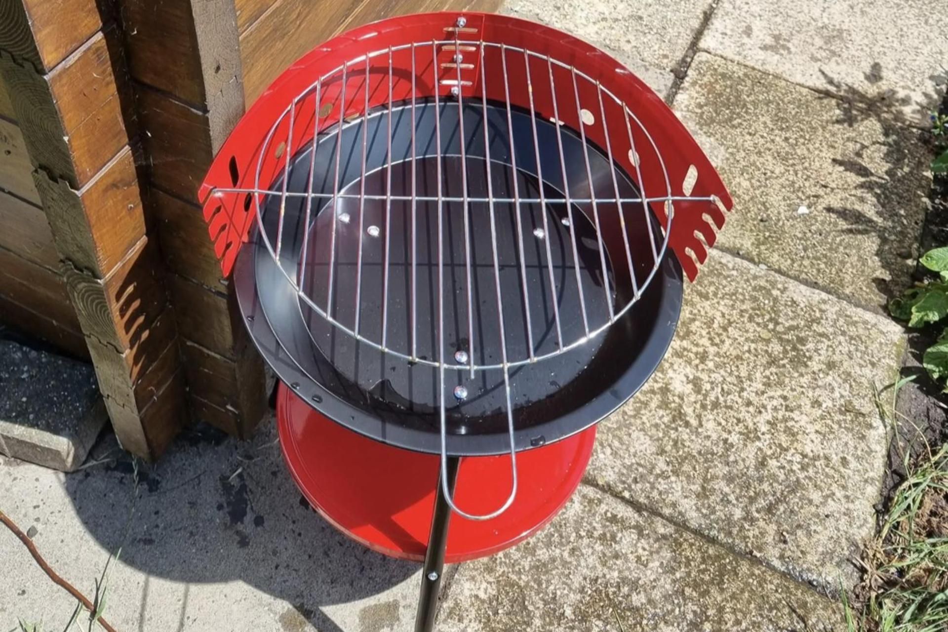 Ein roter Grill mit einem Metallrost auf einer Betonfläche.