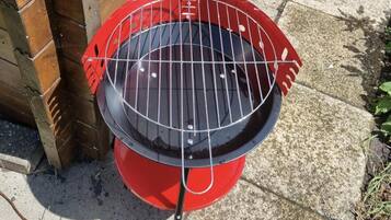 Ein roter Grill mit einem Metallrost auf einer Betonfläche.