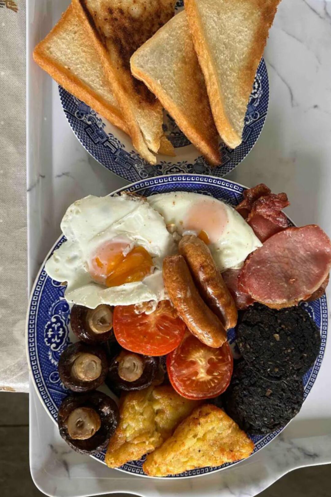 Un piatto da colazione con uova, salsicce, pancetta, funghi, pomodori, sanguinaccio e pane tostato.