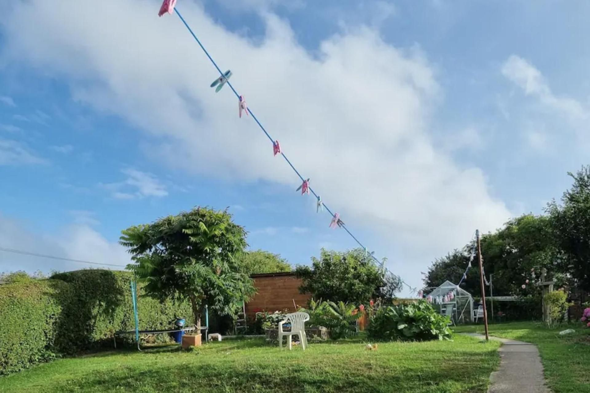 Ett bostadsområde med klar himmel, en rad med tvätt som hänger på en torklina och en trädgård med ett förråd och en stol.