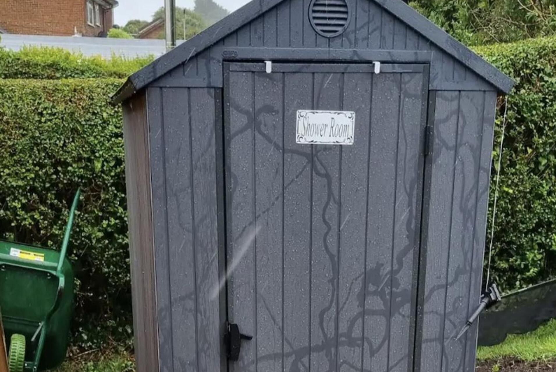 Un abri de jardin gris avec une pancarte indiquant « Salle de douche ».