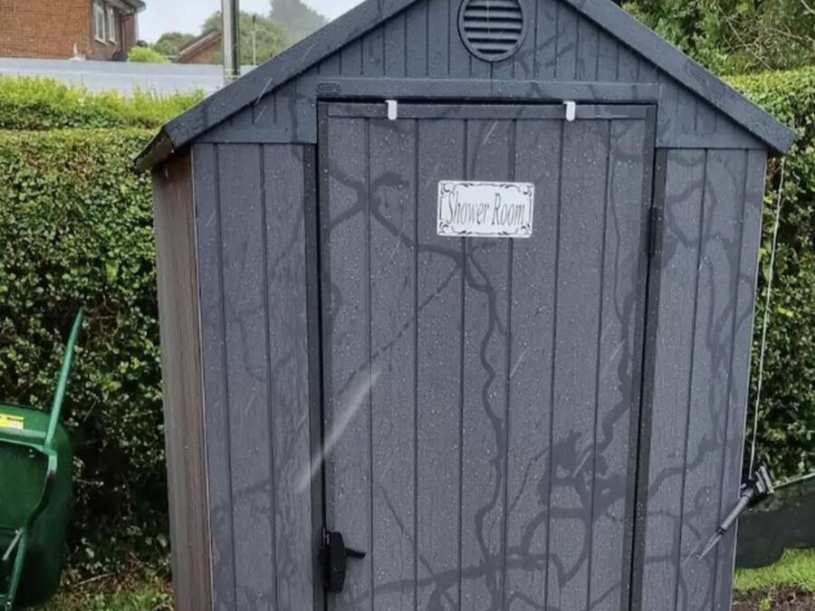 Eine graue Gartenhütte mit einem Schild, auf dem „Duschaum“ steht.