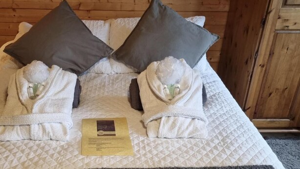 Un lit bien fait, avec deux serviettes pliées en forme de peignoir, un oreiller et une petite carte posée sur le lit.