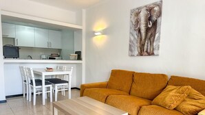 A modern living room with a mustard sofa, a wooden coffee table, and a dining area with white chairs and a small table.