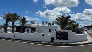 A sign for Villa Blanca, a white building with palm trees, and a clear blue sky with clouds.