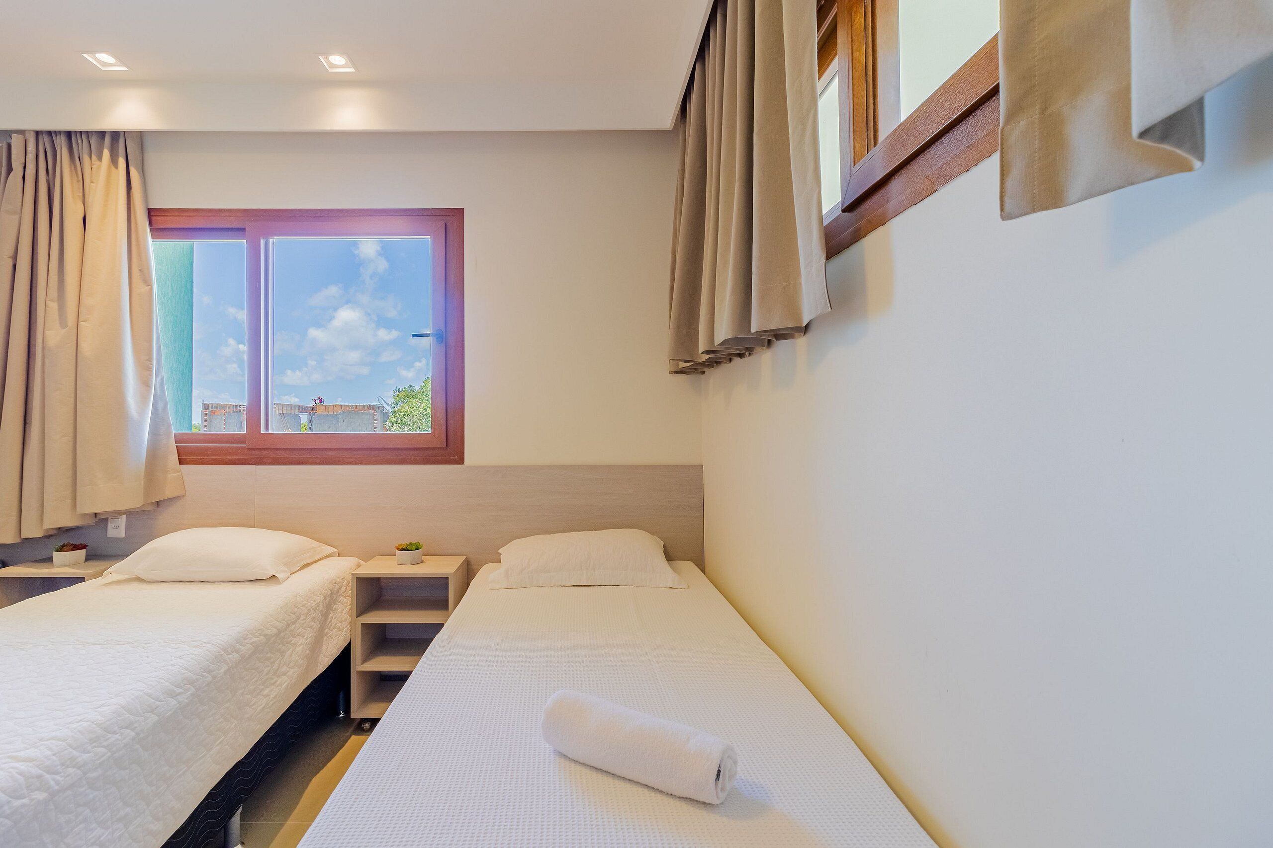 Habitación de hotel con dos camas individuales, una ventana con cortinas, una mesita y una mesilla de noche.