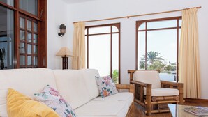 A room with a white sofa, a wooden chair, and large windows with curtains.