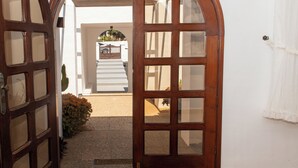 An arched wooden door leading to a white-walled interior with a staircase and a vehicle parked outside.