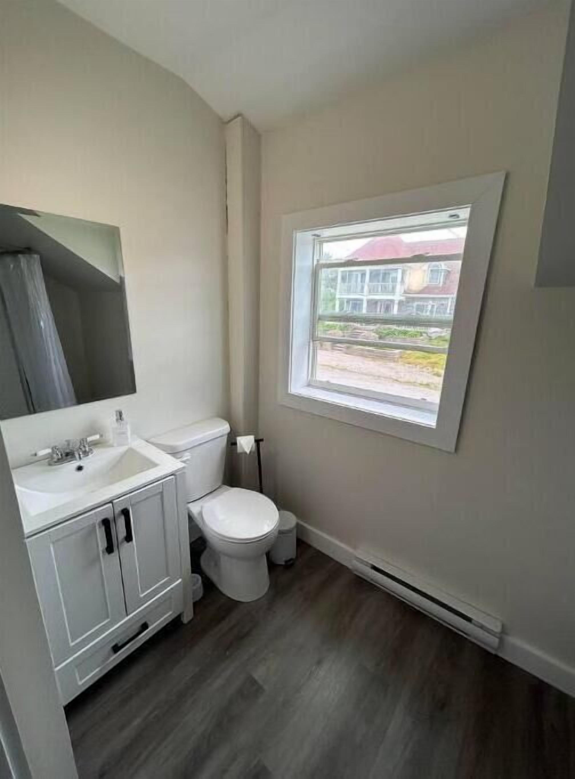 A small, clean bathroom with a toilet, sink, and mirror. There is a window providing natural light.