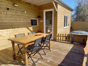 A wooden cabin with a dining table and chairs, a small porch, and a hot tub.