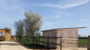 A rustic wooden building with a dirt path leading to it, surrounded by trees and open fields. - Chalet en Ferme Équestre au Plus Proche des Chevaux (Yèvres)