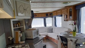 A compact RV interior with a kitchenette, a dining area, and a seating space. - Chalet en Ferme Équestre au Plus Proche des Chevaux (Yèvres)