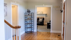 A hallway with a wooden staircase, a black metal shelf with decorative items, a fireplace, and a couch in the background. - Large colonial style house in the most sought after area - Ballantyne.  (Charlotte)