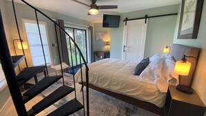 A bedroom with a bed, a TV, a ceiling fan, and a staircase. - Table Rock Lakeview Home Retreat: Stunning Sunsets, Close to Eureka Springs (Holiday Island)