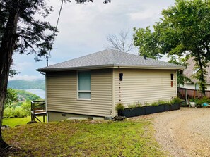 A single-story house with a view of a lake, a deck, and a gravel driveway.