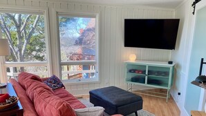A living room with a red sofa, a blue ottoman, a TV mounted on the wall, and a green cabinet. - Table Rock Lakeview Home Retreat: Stunning Sunsets, Close to Eureka Springs (Holiday Island)