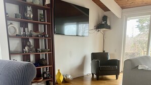 Una sala de estar con piso de madera, un televisor montado en la pared, una estantería y dos sofás.