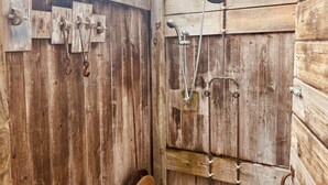 Ducha exterior de madera con varios grifos y cabezal de ducha manual.