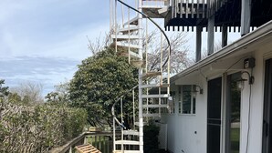 Una terraza de madera con sillones de descanso y una escalera espiral que lleva a un balcón.