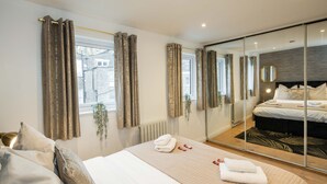 Quarto de hotel moderno com uma cama grande, um espelho e vista para a cidade pela janela.