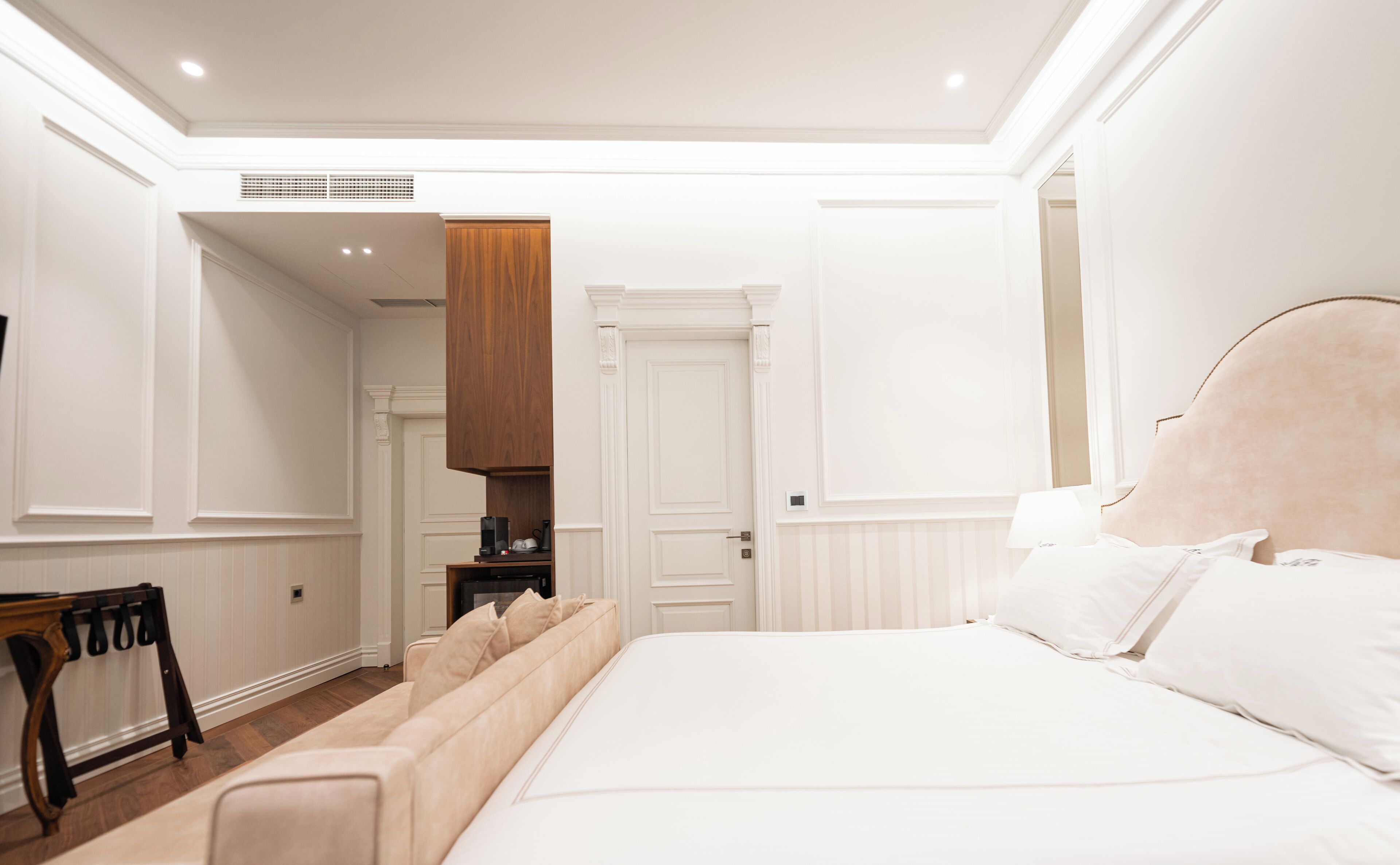 A bedroom with a large bed, a wooden wardrobe, a small table, and a chair.