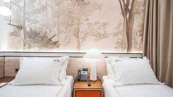 A hotel room with two beds, a nightstand with a lamp, a phone, and a window with a forest view.