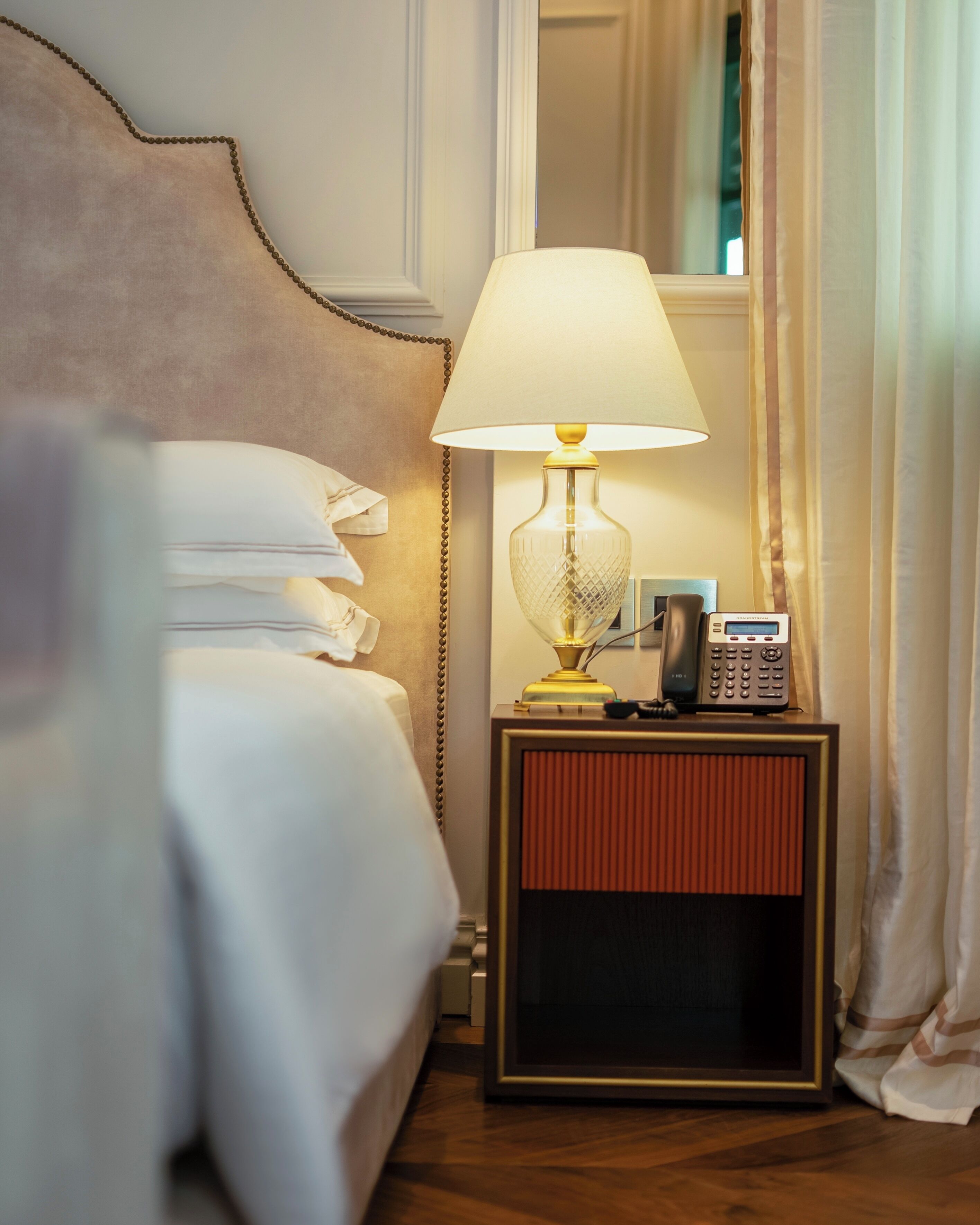 Una cama bien hecha con almohadas, una lámpara de noche, un teléfono y una mesita con una radio.