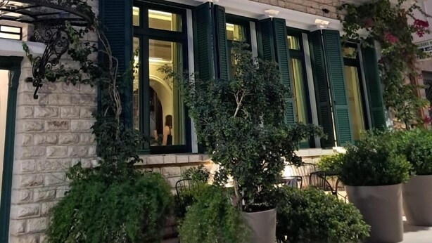 A two-story building with a brick facade, green shutters, and a balcony with a wrought iron railing. - La Fe boutique Hotel Sarande (Sarandë)