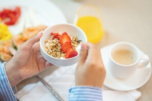 Ein Frühstückstisch mit einer Schüssel Müsli, belegt mit Erdbeeren, einer Tasse Kaffee und einem Glas Orangensaft.