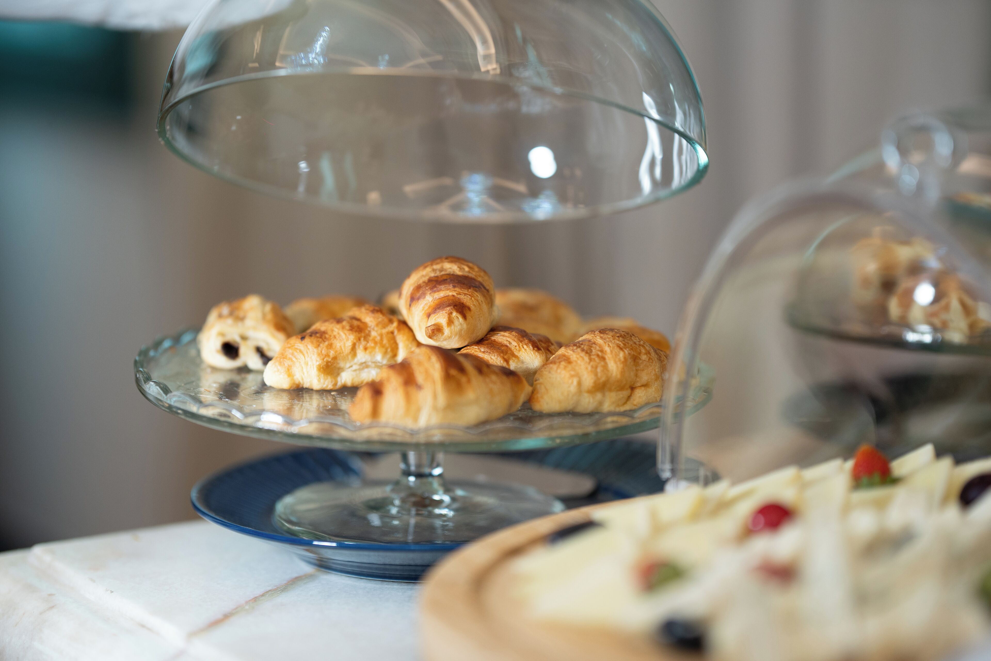 A glass display case with pastries, including croissants and a cake with fruit toppings.