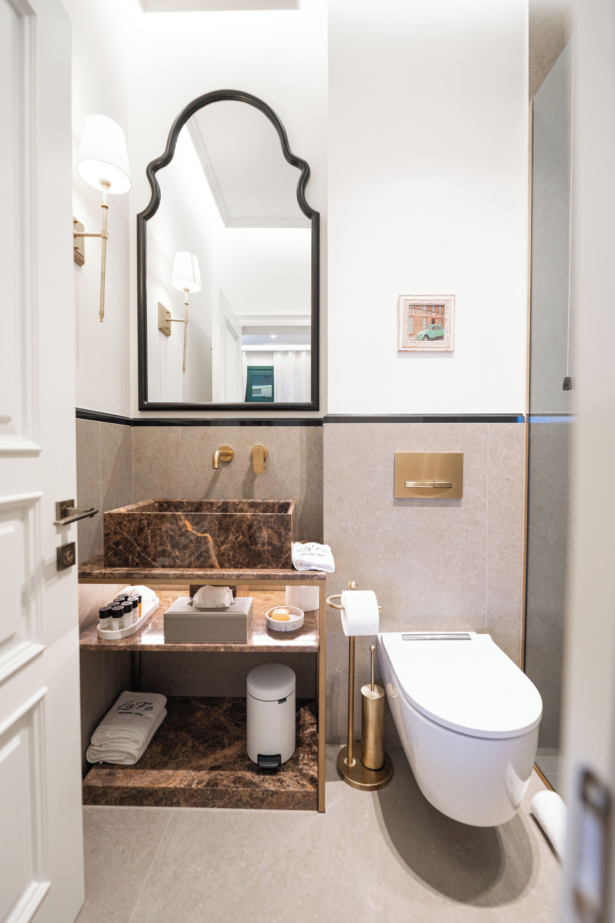 Une salle de bain moderne avec un lavabo en marbre, un grand miroir, des toilettes et un petit tableau encadré accroché au mur.