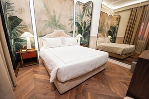 Habitación de hotel con una cama grande, dos mesitas de noche con lámparas, un espejo y un piso de madera con motivo de espiga.