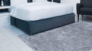 Une chambre moderne avec un grand lit, deux tables de chevet avec des lampes, un fauteuil rembourré de couleur sombre et une tête de lit à motifs géométriques.