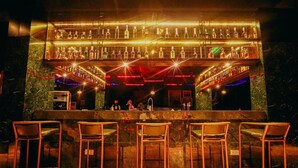 Un espace bar doté de plusieurs étagères remplies de bouteilles, d’un comptoir et de quatre tabourets de bar.