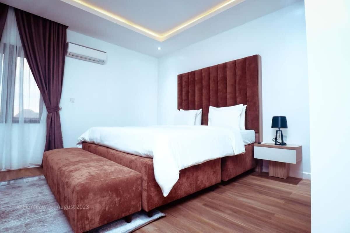 A modern bedroom with a large bed, a bedside table with a lamp, and a window with curtains.