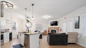A modern kitchen with a central island, a dining area with a sofa, a fireplace, and a TV mounted above it. - Newly renovated Blue Mountain condo in Historic Snowbridge (The Blue Mountains)