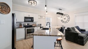 A modern kitchen with a central island, stainless steel appliances, and a dining area with a dark sofa and bar stools. - Newly renovated Blue Mountain condo in Historic Snowbridge (The Blue Mountains)