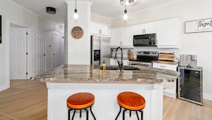 A modern kitchen with white cabinetry, granite countertops, stainless steel appliances, and two bar stools. - Newly renovated Blue Mountain condo in Historic Snowbridge (The Blue Mountains)