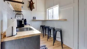 Une cuisine moderne avec un plan de travail en bois, un évier et une décoration murale représentant une tête de vache. On y trouve trois tabourets noirs et une fenêtre qui laisse entrer la lumière naturelle.